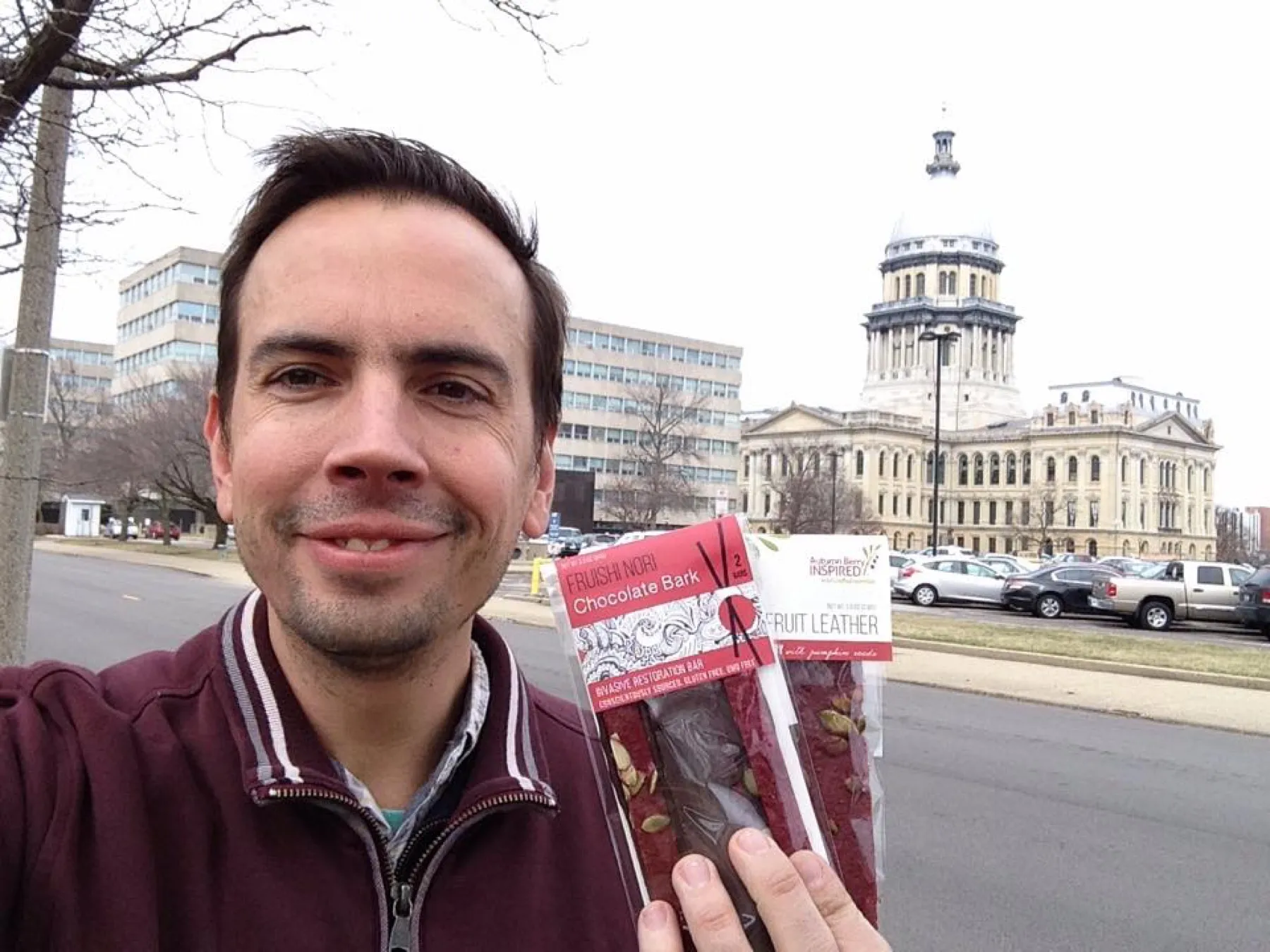 Dustin Kelly holding a package of fruit leather in front of the Illinois State Capitol dome.