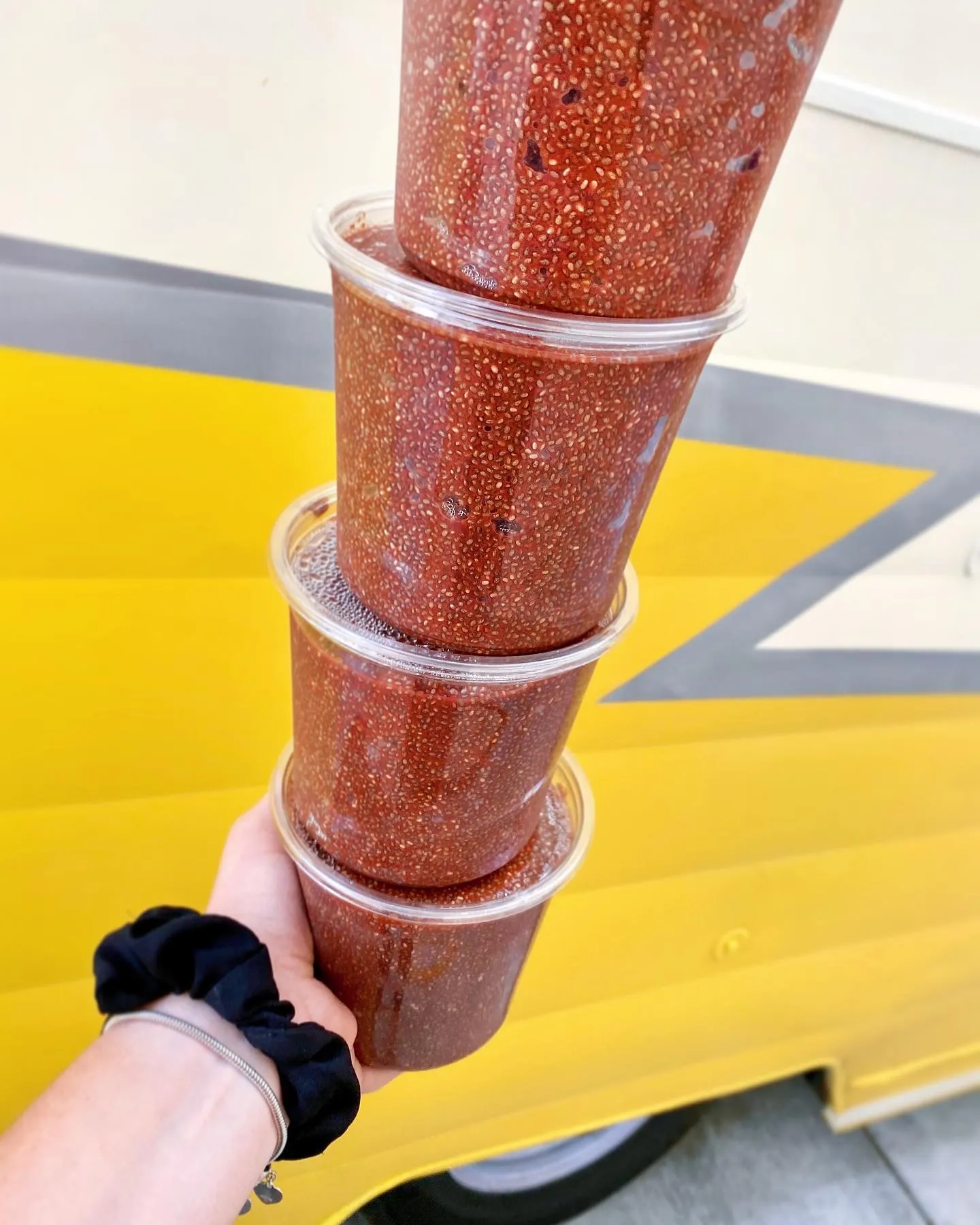 A stack of clear cups of autumn berry chia pudding held up against a yellow food truck.