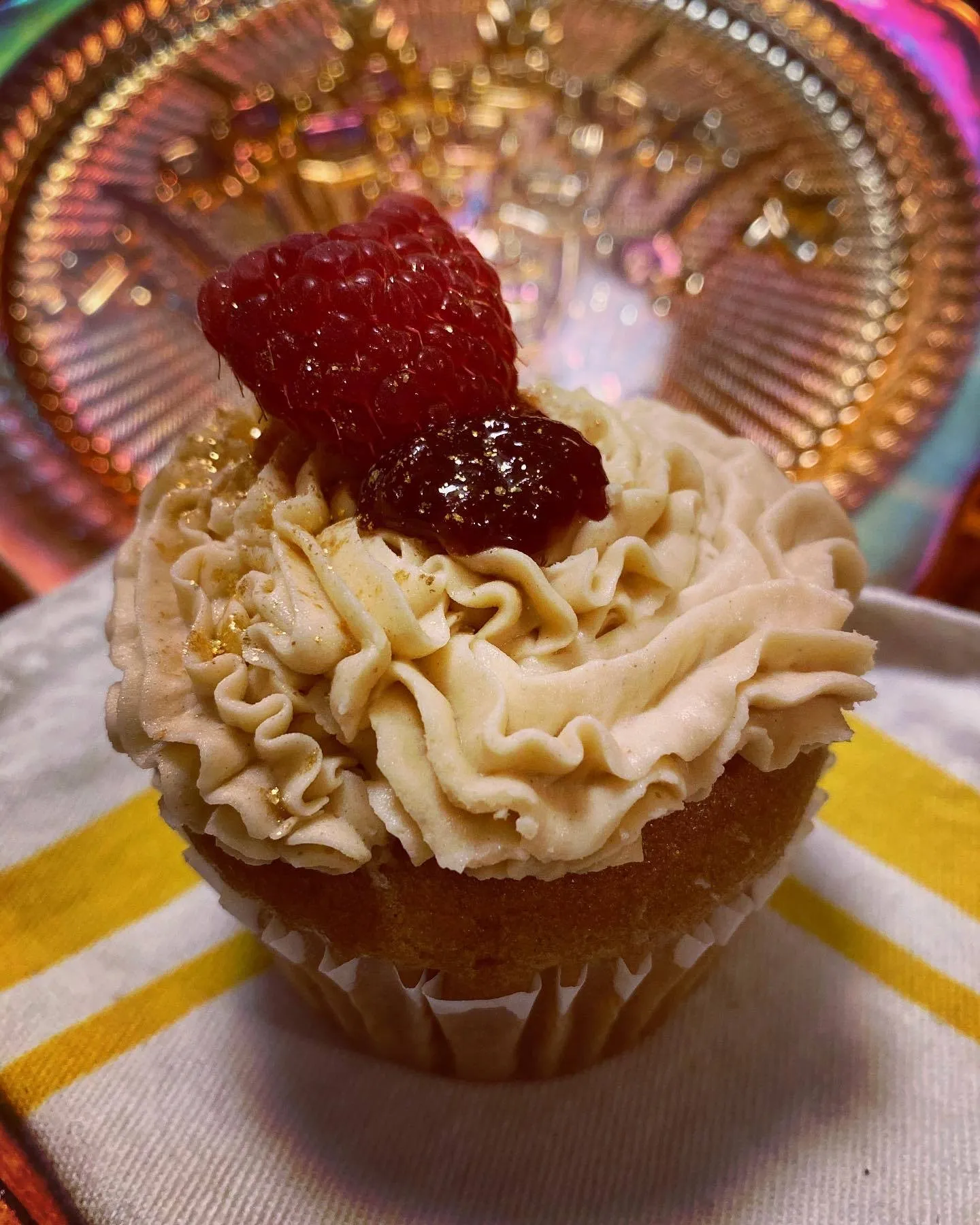A cupcake topped with cream frosting and a cube of red autumn berry jelly.