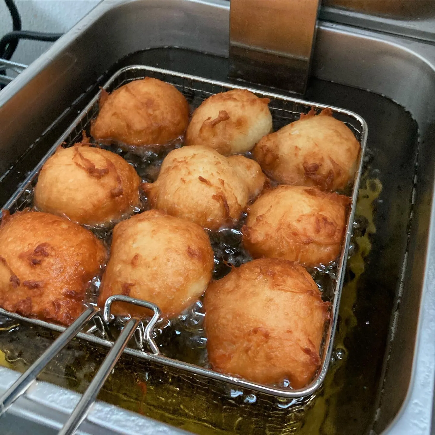 Golden malasadas frying in a basket of hot oil.