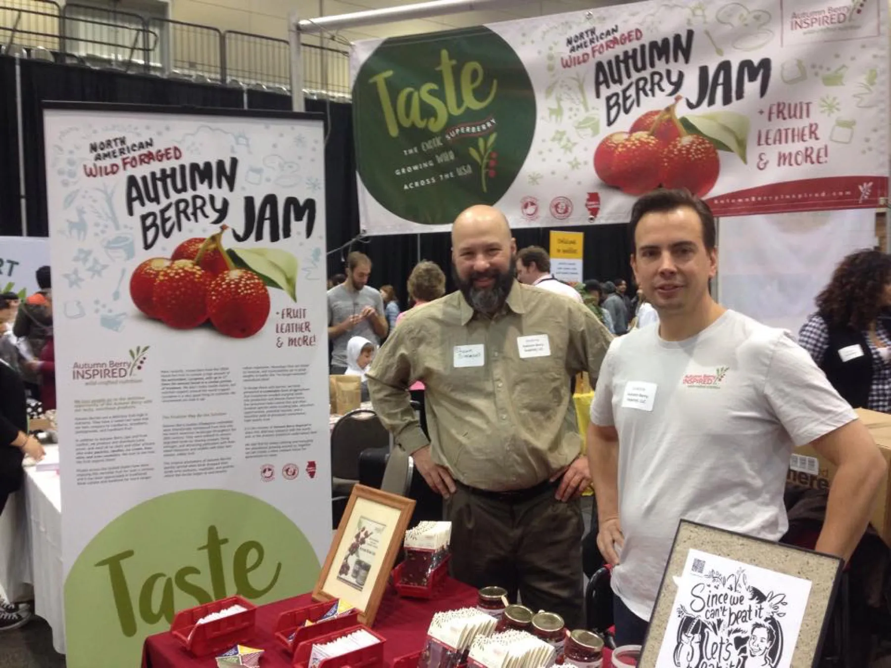 Dustin Kelly and a colleague at a trade show booth with Autumn Berry Jam banners reading Taste.
