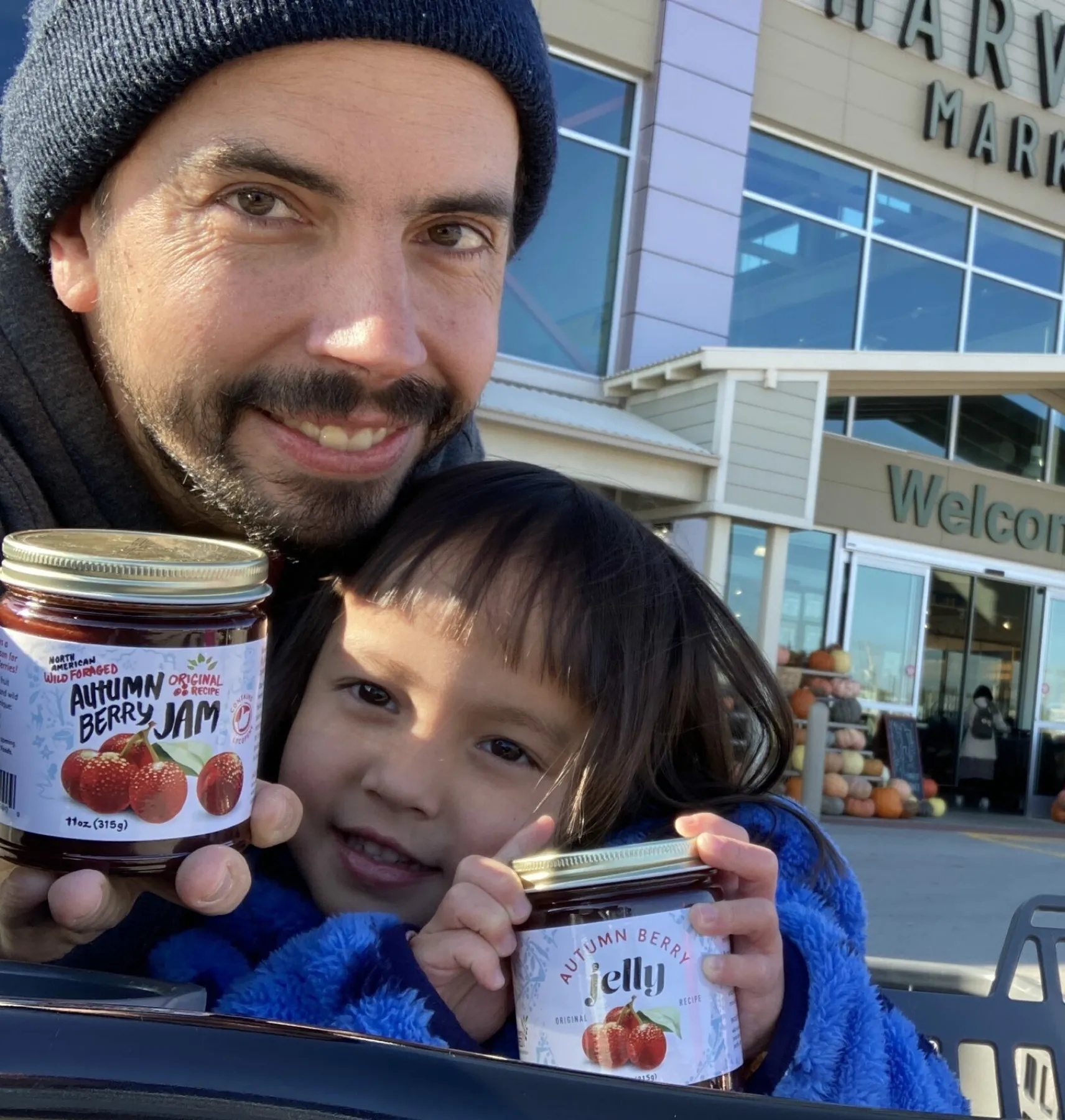 Dustin Kelly and his young daughter holding jars of autumn berry jam outside Harvest Market.