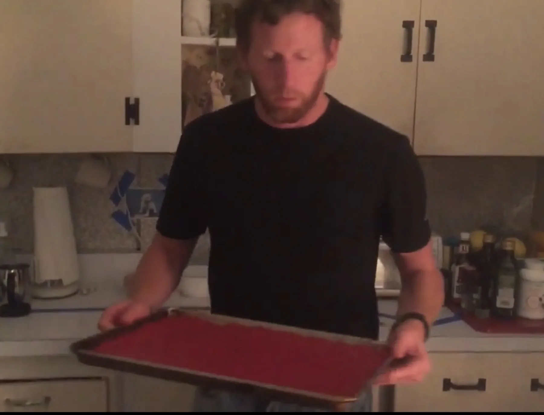 A cook carrying a sheet pan of spread red fruit puree in a home kitchen.