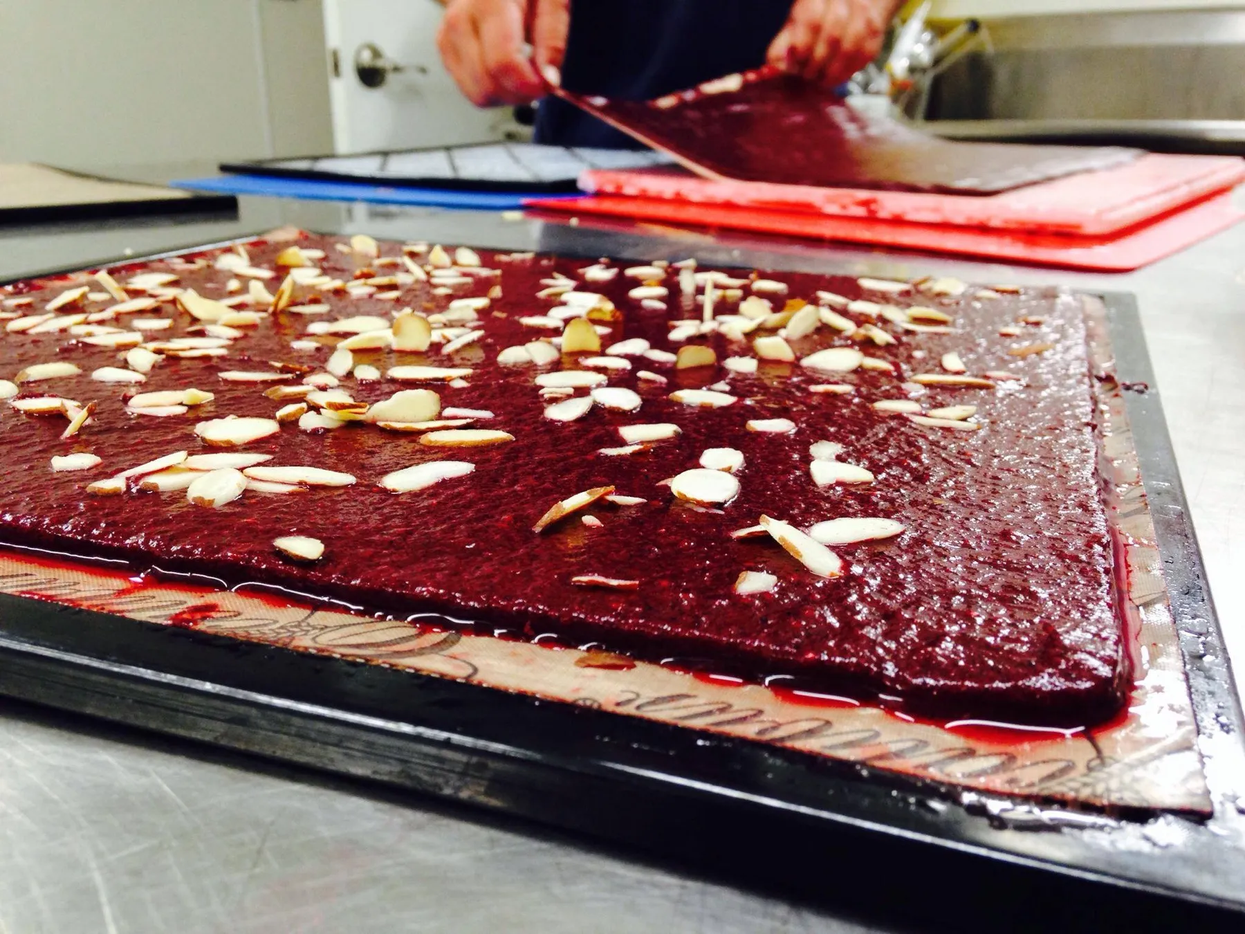 A tray of freshly spread autumn berry fruit leather topped with sliced almonds, being cut into strips.