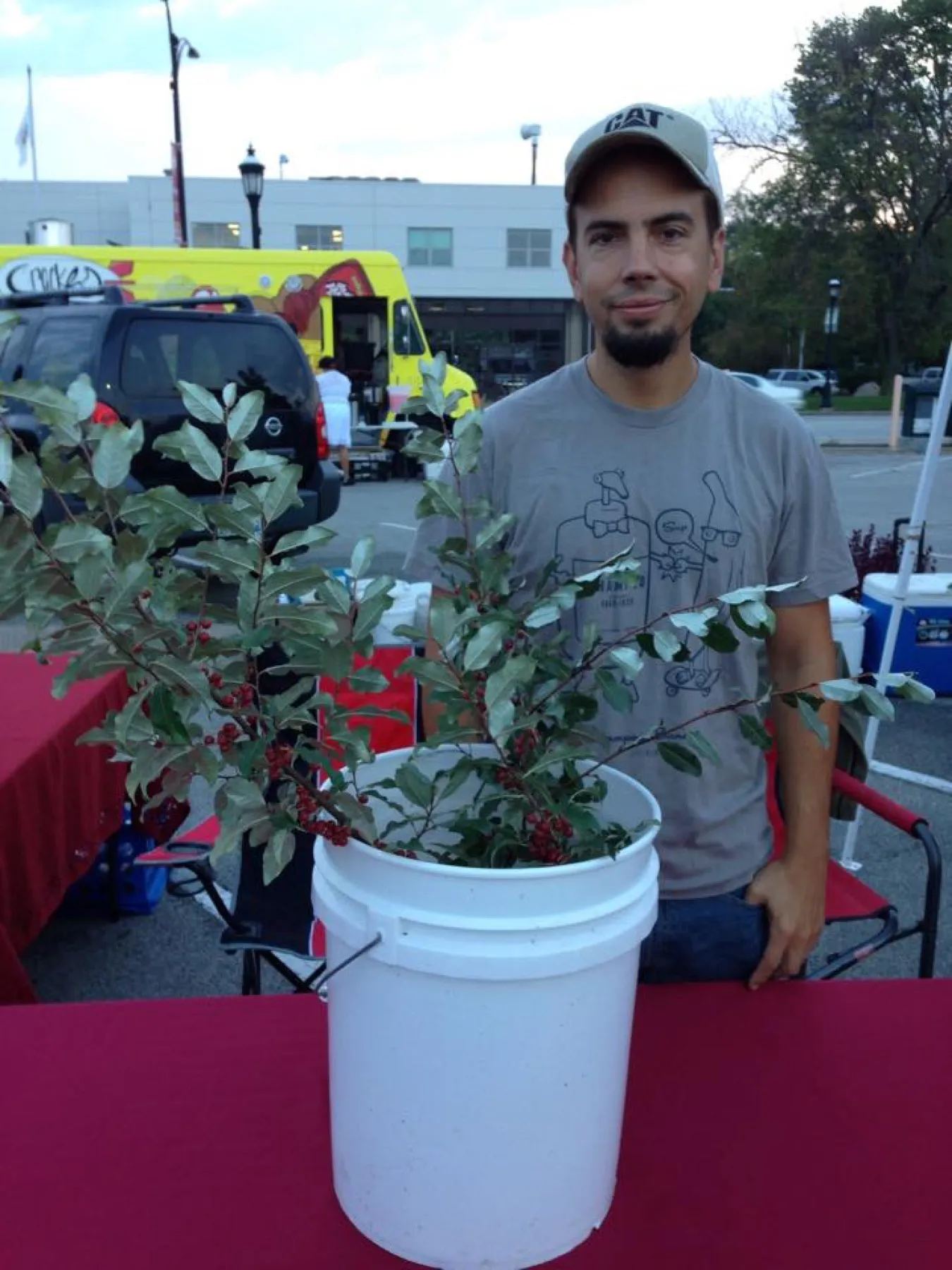 Dustin Kelly at a market stall beside fruiting autumn olive branches displayed in a white bucket.