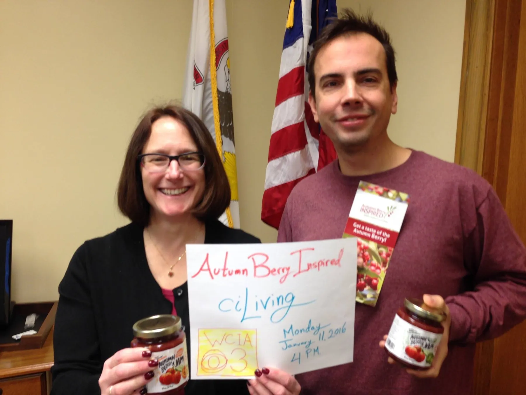 Dustin Kelly and Champaign Mayor Deb Feinen holding jars of autumn berry jam and a handwritten sign.