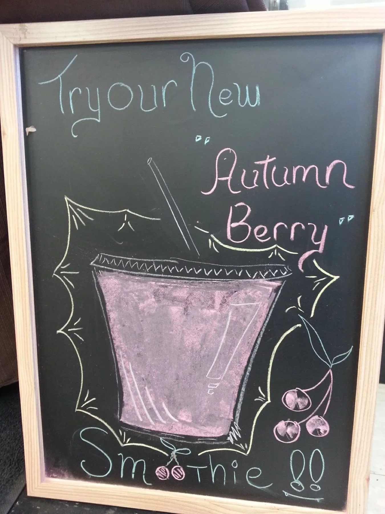 A chalkboard sign reading Try our new Autumn Berry smoothie, with a drawing of a pink drink.